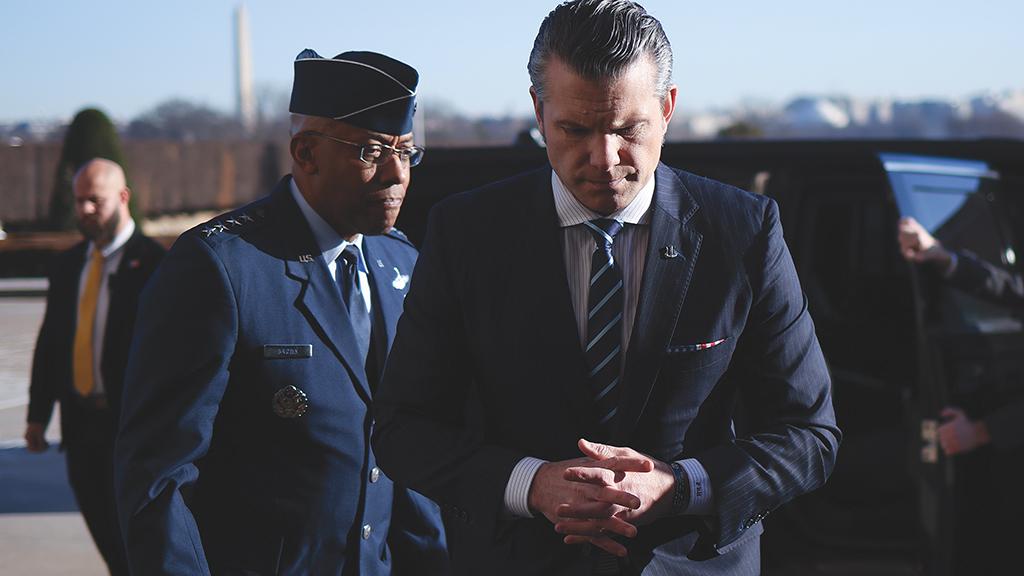 Pete Hegseth looking down and clasping hands with Gen. Charles Q. Brown, Jr., to his left